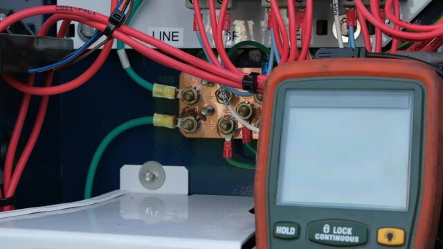 An Engineer With A Gloved Hand Connects A Wire With A Plug To The Panel With Wires, Digital Values Appear On The Electronic Device. Checking The Circuit For Electrical Breakdown.