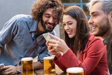 Young people using mobile phone and having fun drinking beer at brewery bar - Happy friends dinning lifestyle concept