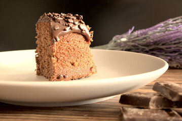 Slice of homemade chocolate cake on wooden background, with pieces of chocolate on the side