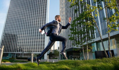 successful man in formalwear running with computer outside the office, hurry up