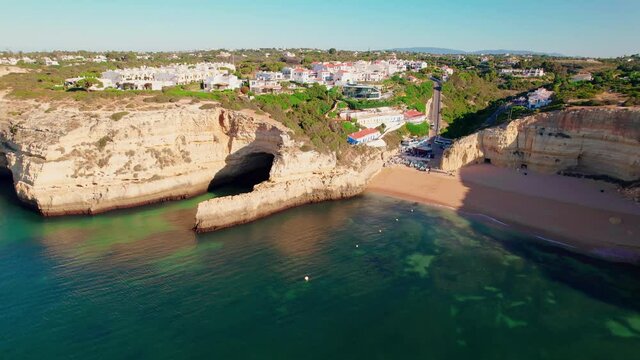 Aerial view of Benagil Beach, boats and vessels, hotels and restaurants in 4K. Benagil, Carvoeiro from above, a coastal tourist Village in Algarve popular of all the maritime caves in Portugal.