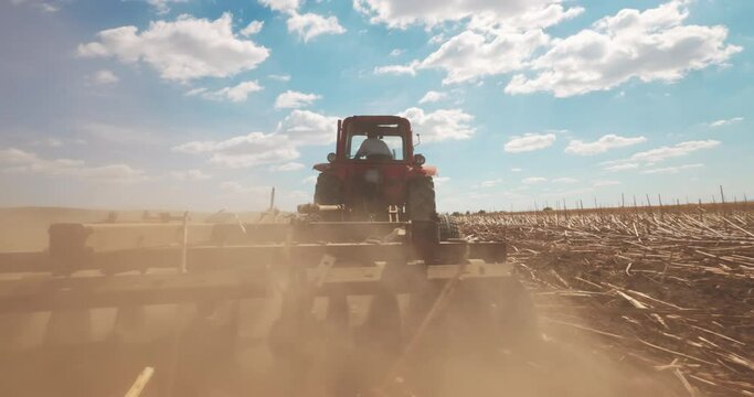 Agricultural Tractor Ploughing Field. Harrow. Farmer in tractor preparing land for sowing