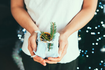 Man holding hand-made eco-friendly wrapped Christmas gift box decorated with a fir tree branch and dried orange. Zero waste holidays. Furoshiki packaging.