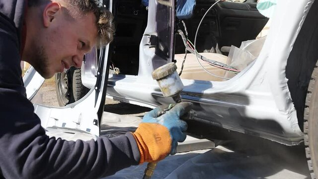 man covers the body  car with a primer, preparing for painting. Anti-corrosion treatment of the car body.