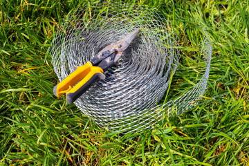 A roll of reinforced mesh for construction and wire cutters lie on the grass. Horticultural use to...