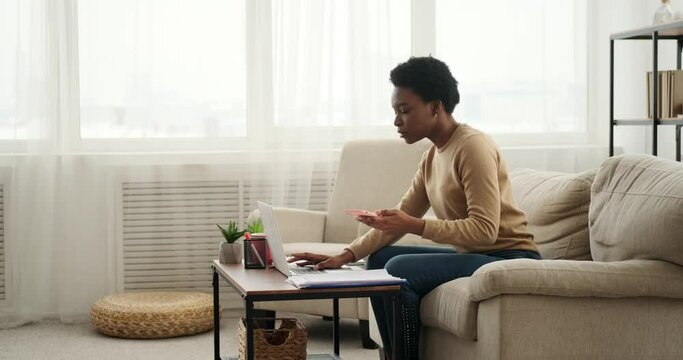 Woman analyzing documents while using laptop and talking on mobile phone at home
