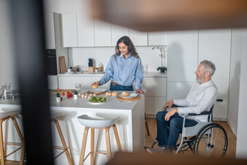 Young dark-haired woman preparing breakfast for her disabled husband