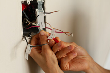 An electrician is replacing a wall switch. A DIY project concept. High voltage danger. She is...