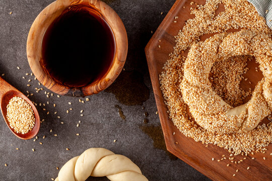 delicious Turkish bagel with sesame seeds known as susamli simit.  Woman baker is making it using twisted dough dipped into a bowl of pekmez and sesame seeds.