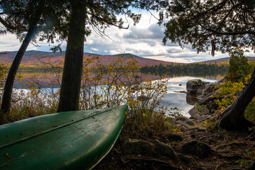 A canoe perched along the lakeshore in Maine during peak foliage season.  - 463936685