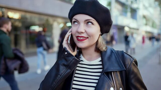 Young pretty woman talking on mobile phone on busy street. Lady smiling, flirting with her interlocutor. Autumn season. Technology, connection concept.