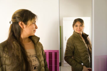 joven mujer morena feliz frente al espejo probándose o eligiendo ropa de abrigo con enfoque...