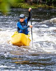 Fototapeta na wymiar A solo canoeist practices on a rainy fall day during a “moving water” paddling course. Shot at Palmer Rapids on the Madawaska River an iconic paddling destination in Eastern Ontario, Canada