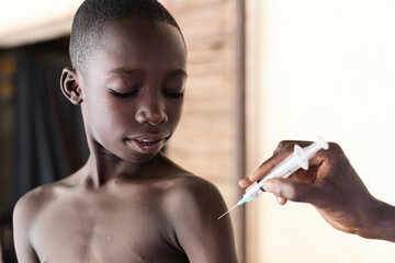 Black nurse explaining injection tool to a young attentive looking African schoolboy during...
