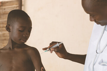 Doctor explains to a small confident looking black boy what happens during malaria vaccination