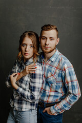 young couple in plaid shirts hugs on gray background