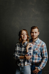 young couple in plaid shirts hugs on gray background