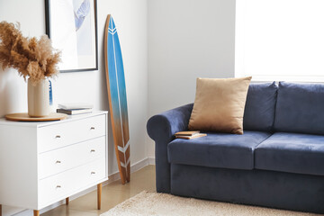Interior of modern stylish room with chest of drawers, sofa and surfboard
