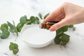 Woman adding essential oil to water in bowl on white background