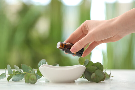 Woman Adding Essential Oil To Water In Bowl On Table