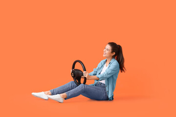 Young woman with steering wheel on color background