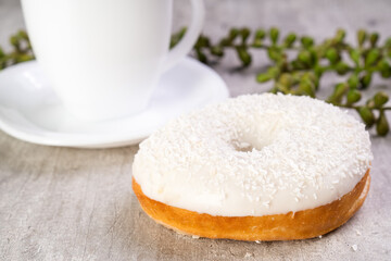Closeup of delicious donut with icing on wooden background and white cup in composition
