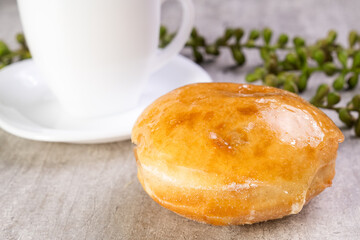 Closeup of delicious donut with icing on wooden background and white cup in composition