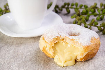 Closeup of delicious donut with icing on wooden background and white cup in composition