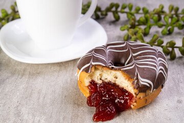 Closeup of delicious donut with icing on wooden background and white cup in composition