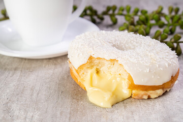 Closeup of delicious donut with icing on wooden background and white cup in composition