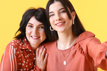 Young woman with her mother taking selfie on yellow background, closeup