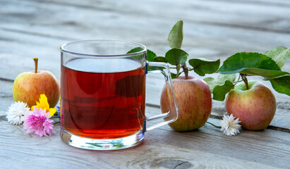 Still life with a glass of tea and apples on a wooden background.