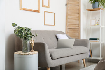 Glass vase with eucalyptus on table near comfy sofa in modern living room