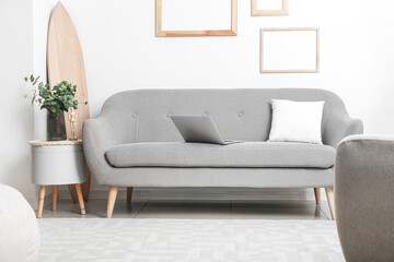 Grey modern sofa and glass vase with eucalyptus on table near light wall
