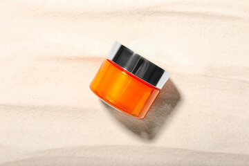 Orange jar of cosmetic product on light sand background