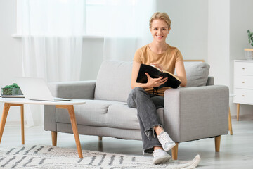 Young woman reading Holy Bible on sofa at home