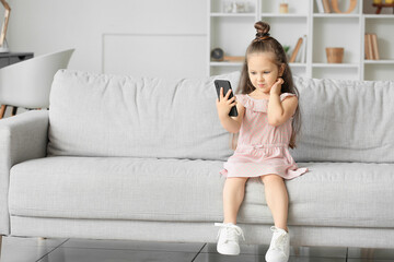 Adorable little girl using mobile phone on sofa at home