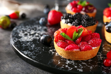 Board with tasty berry tart on dark background