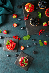 Boards with tasty berry tartlets on dark background