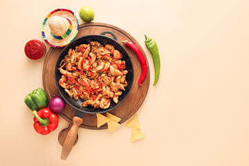 Frying pan with tasty Fajita, sauce and sombrero hat on color background