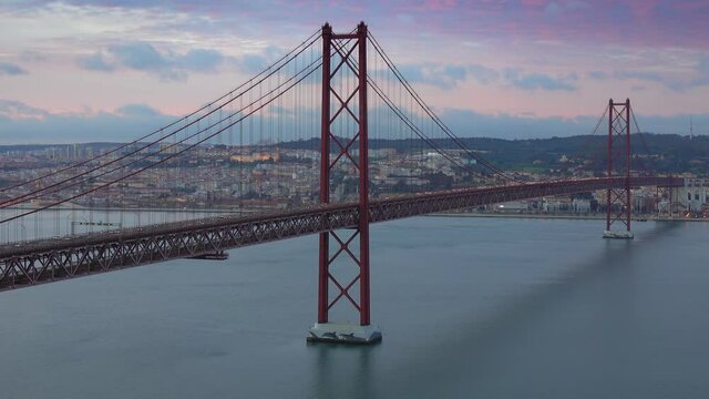 The Bridge of 25th April with car traffic and panoramic view of the city on the background after sunset, Lisbon, Portugal, timelapse 4k
