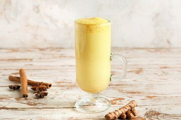 Glass of healthy turmeric latte on light wooden table