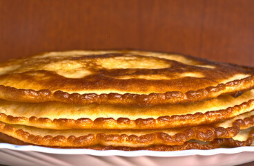 Golden delicious pancakes lie on a plate on top of each other.