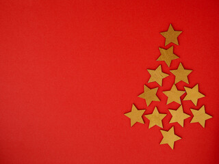 Naklejka na ściany i meble Christmas tree made from golden wooden holiday star shaped decoration. Red paper background. Vintage style. Greeting card poster template. Creative review concept. Flat lay, top view, copy space