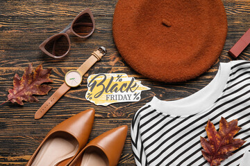 Trendy female clothes, accessories, dry leaves and text BLACK FRIDAY on wooden background