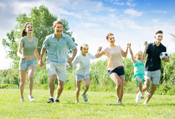 cheerful family happily playing and running together outdoors on green meadow