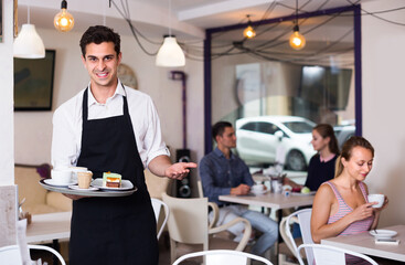 Fototapeta na wymiar Male waiter is warmly welcoming guests to cozy coffeehouse.