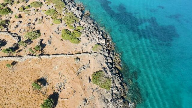 Top down aerial view of a rocky coastline and crystal clear ocean in Elounda, Crete