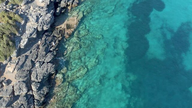Top down aerial view of a rocky coastline and crystal clear ocean in Elounda, Crete