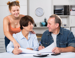 Fototapeta premium Smiling parents are reading utility bill with their adult daughter at home.